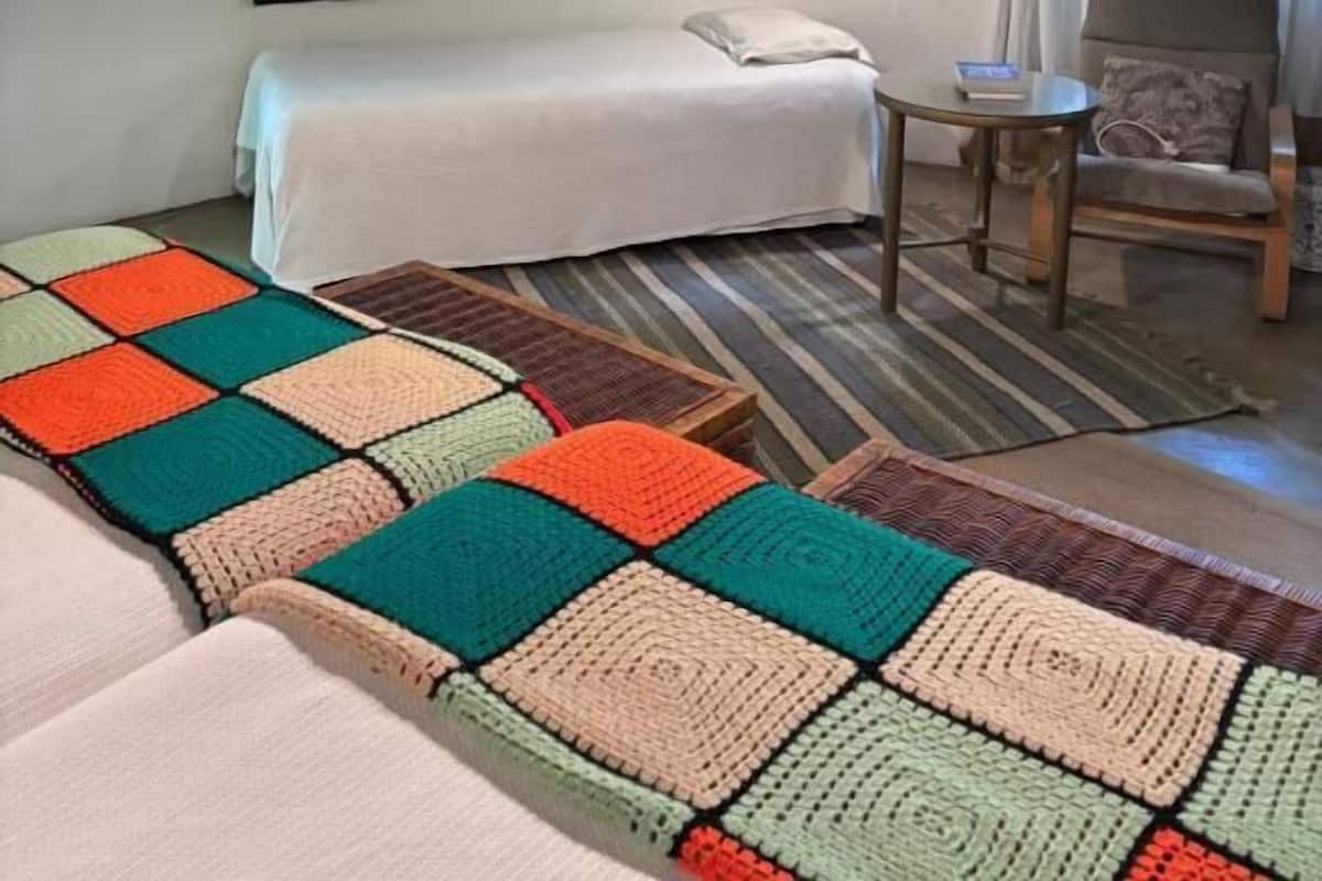 Una habitación con cama, dos lámparas colgantes, un cuadro, una silla y un tapete colorido.