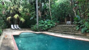 A swimming pool with steps leading up to a patio area with white lounge chairs and a table. - Old Joe's Kaia (Mbombela)