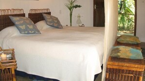 A bedroom with a bed, two bedside lamps, a painting, a potted plant, and a view of greenery through a door. - Old Joe's Kaia (Mbombela)