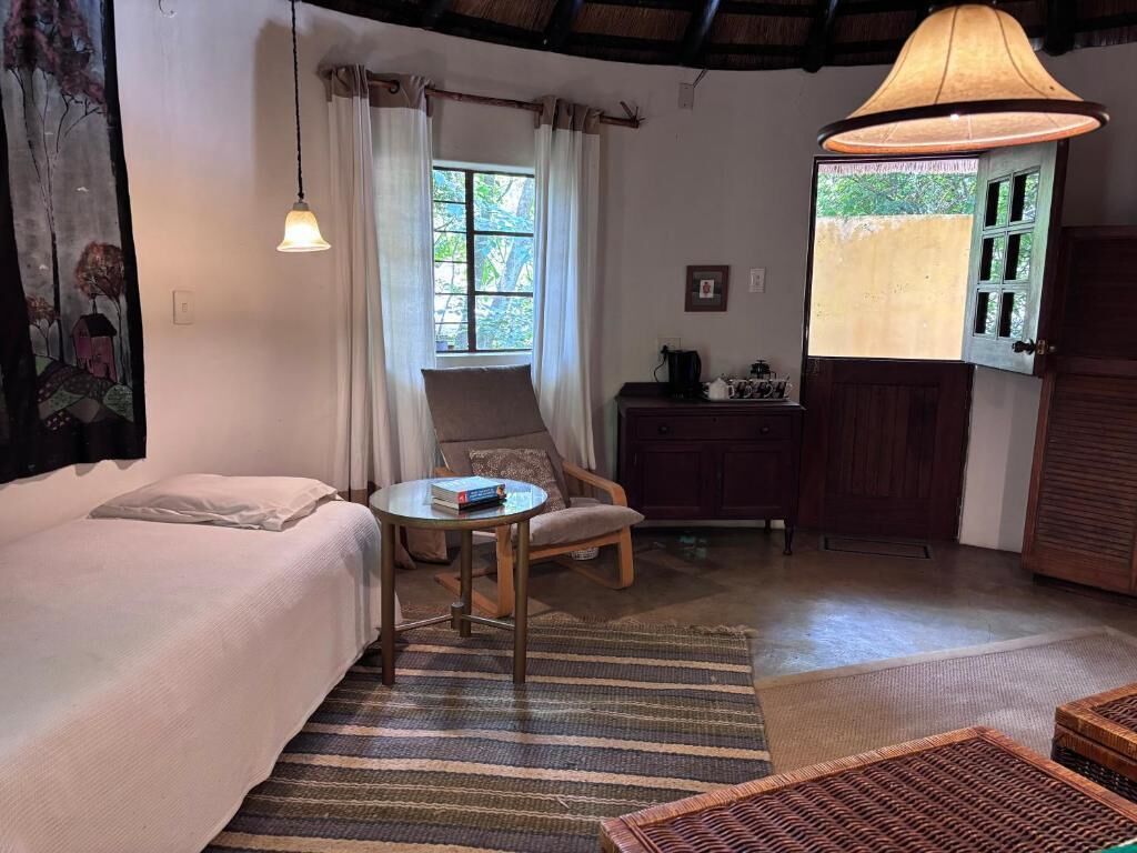 Una habitación acogedora con cama, una mesita, una silla, una lámpara colgante y vistas al verdor exterior.