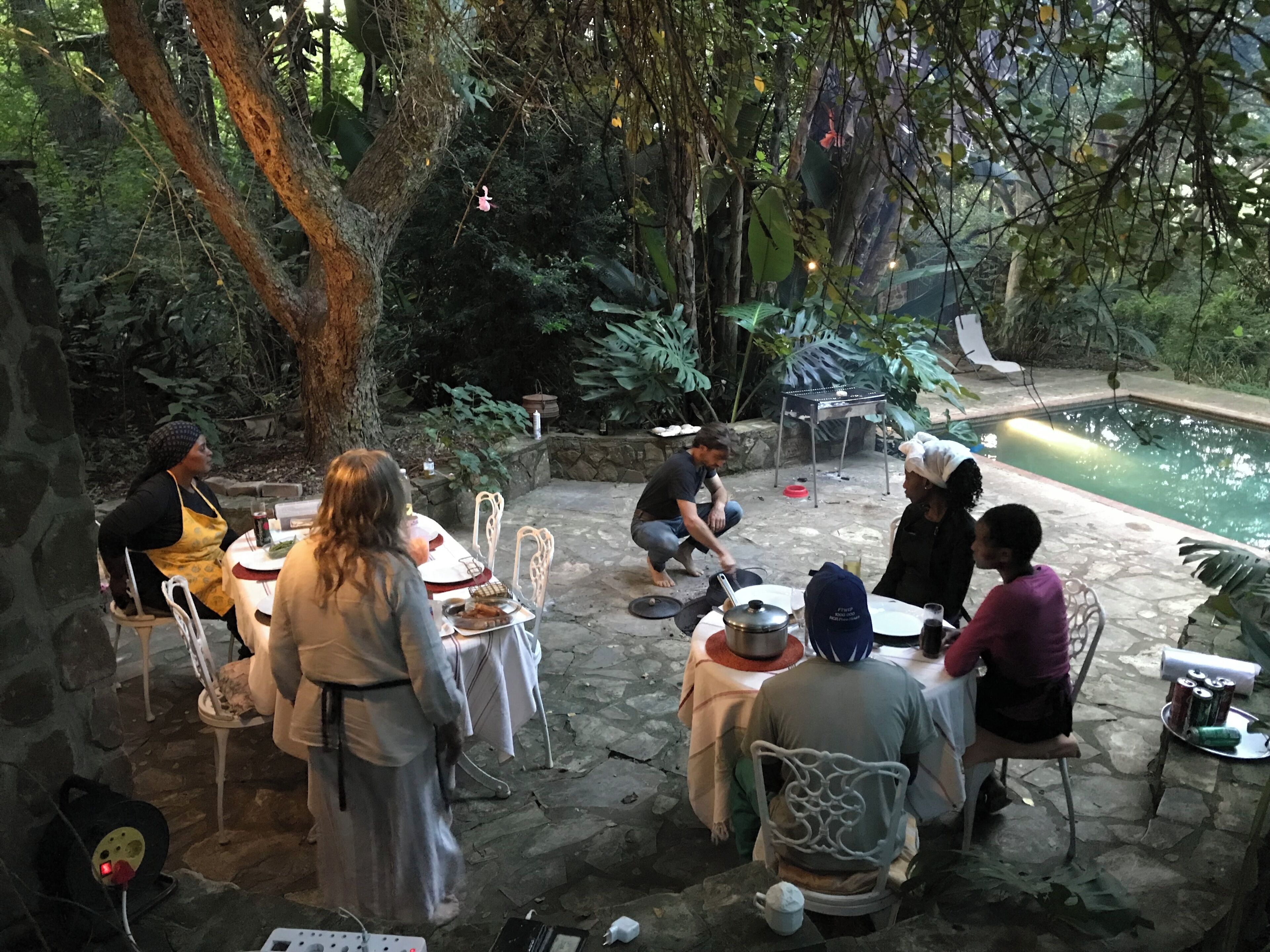 Un espace extérieur aménagé pour les repas, doté d’un sol en pierre, entouré d’une végétation luxuriante et agrémenté d’une piscine.