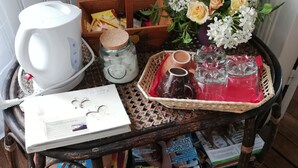 Un carrito de madera con una tetera blanca, un tarro de cristal, una cesta de flores, una bandeja con tazas y una revista.