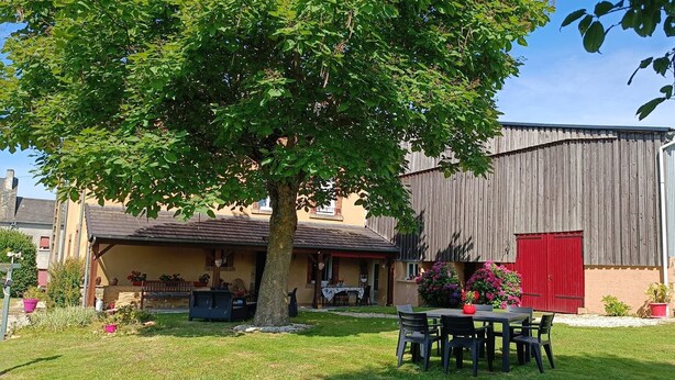 Un espacio de estar al aire libre rústico con una mesa, sillas, un árbol y un edificio con puerta roja.