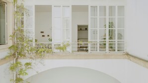 Een wit gebouw met open ramen en deuren, een balkon met planten en een zicht op het interieur.