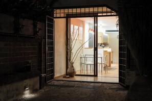 A doorway leading into a room with a dining area, a vase with branches, and a brick wall.