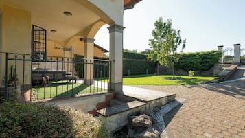 Eine überdachte Terrasse mit einer Steinsitzbank, einem Metallzaun und einem gepflegten Rasen.