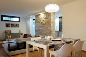 A modern living room with a dining area, stone accent wall, and a chandelier.