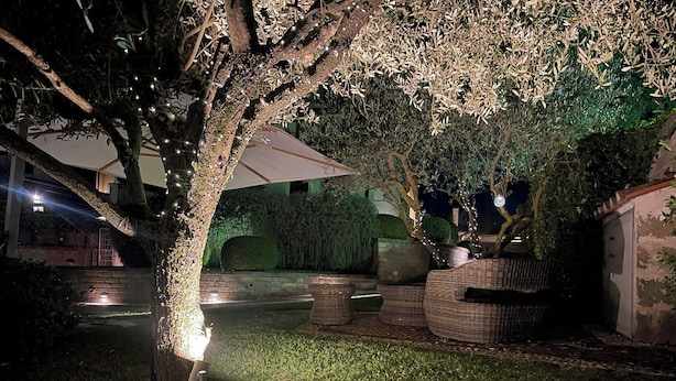 An outdoor area with a large umbrella, wicker furniture, and a tree with lights. - Villa with pool at Lake Bracciano (Bracciano)