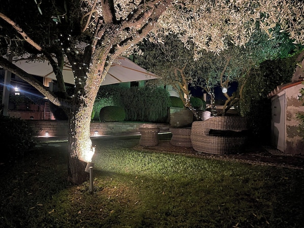 An outdoor area with a large umbrella, wicker furniture, and a tree with lights.