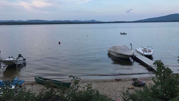 A calm lake with boats docked at the shore, surrounded by mountains.