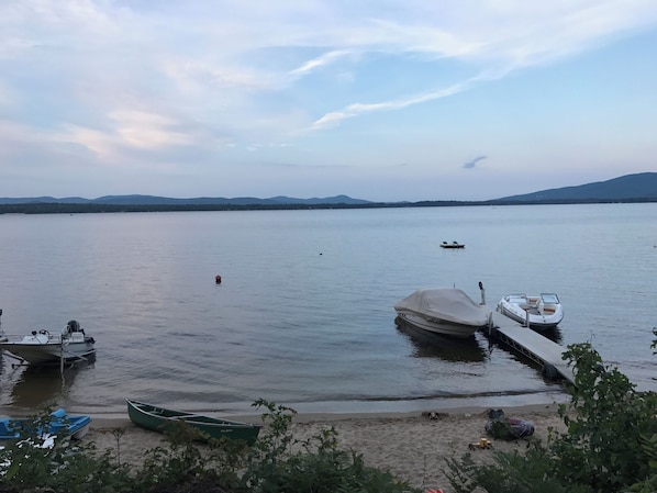 A calm lake with boats docked at the shore, surrounded by mountains.