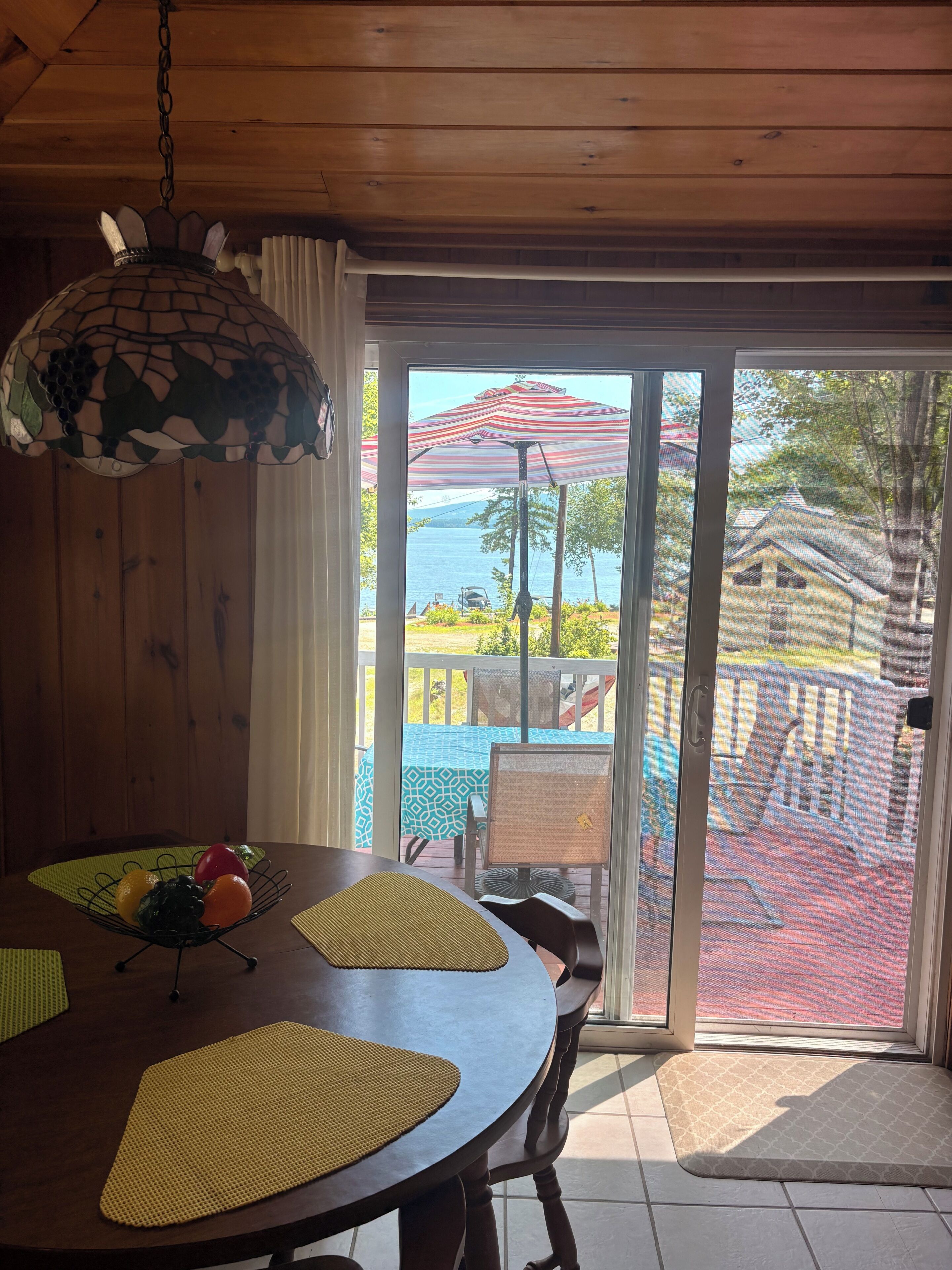 Un tavolo da pranzo in legno con una ciotola di frutta, un lampadario e vista su un patio con mobili da esterno e una casa sullo sfondo.