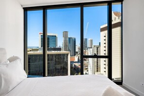 A hotel room with a large bed, white bedding, and a city view through floor-to-ceiling windows. - City Sky Nest - Luxe Apartment with City Views (Perth)
