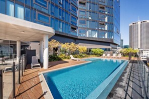 A rooftop pool with lounge chairs, a covered seating area, and a modern building with large windows. - City Sky Nest - Luxe Apartment with City Views (Perth)