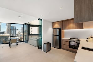 A modern kitchen with a city view, a dining area with chairs, and a small sofa. - City Sky Nest - Luxe Apartment with City Views (Perth)