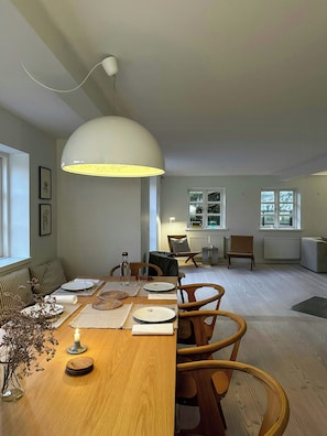 Ein Essbereich mit einem Holztisch, Stühlen, einer Hängeleuchte und Blick zum Wohnzimmer.