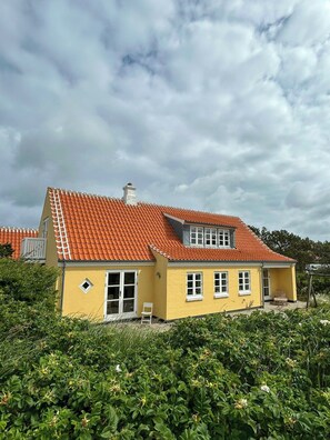 Ein gelbes Haus mit rotem Ziegeldach, weißen Fenstern und einem Schornstein.