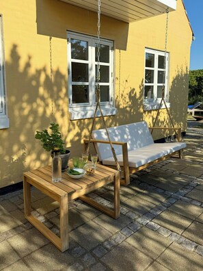Ein Holzschaukelstuhl und ein Tisch vor einem gelben Gebäude mit weißen Fenstern.