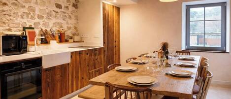 A kitchen with a stone wall, wooden cabinets, a dining table set for six, and a window with a view.