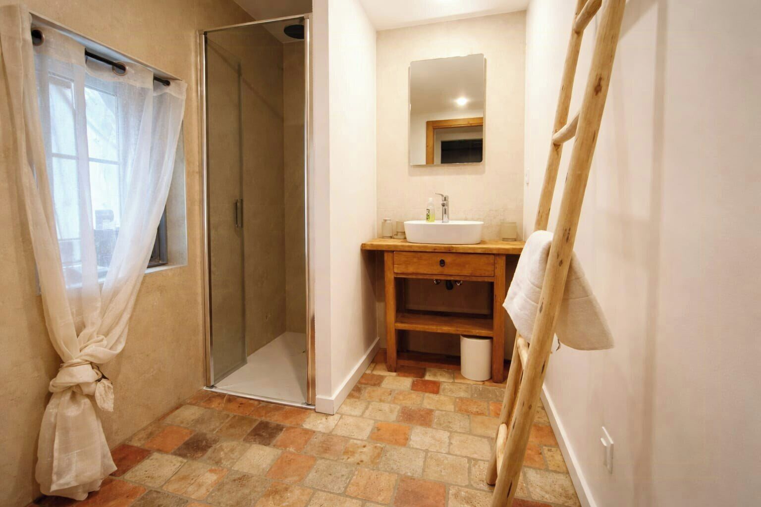 Een badkamer met een douchecabine met glazen deur, een houten wastafelmeubel met een wastafel, een spiegel en een handdoekhouder.