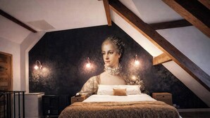 Ein Schlafzimmer mit schrägen Wänden, einem Bett mit gemustertem Überwurf, Nachttischen und Wandleuchten.