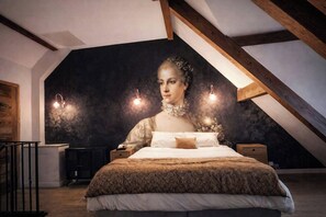 Ein Schlafzimmer mit schrägen Wänden, einem Bett mit gemustertem Überwurf, Nachttischen und Wandleuchten.