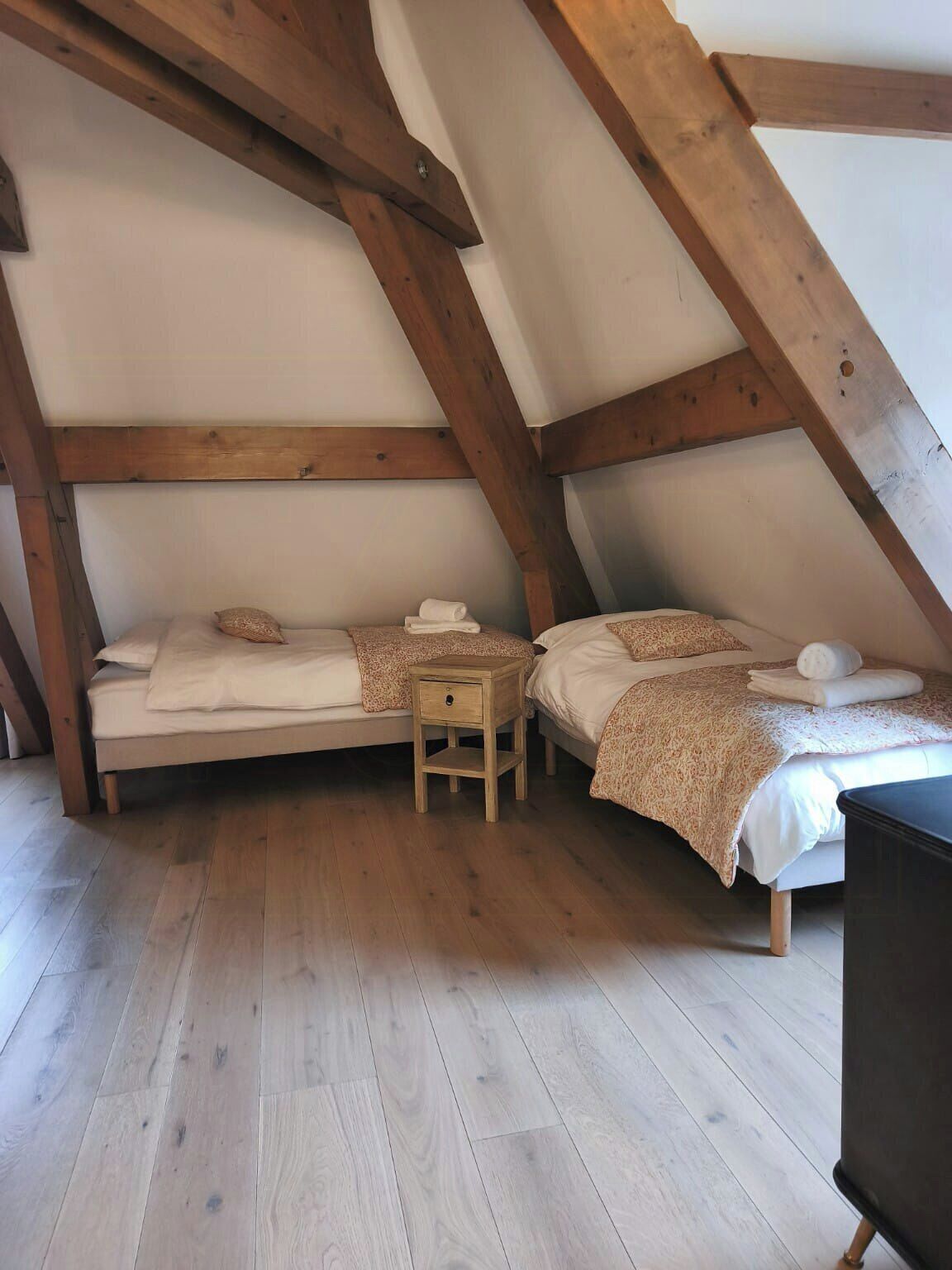 A loft bedroom with two beds, wooden beams, and a small wooden nightstand.