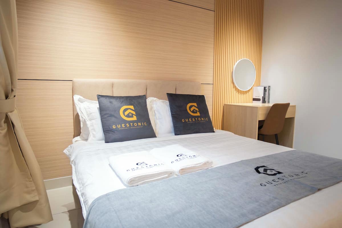 A hotel room with a bed, a desk, a chair, a round mirror, and a robe.