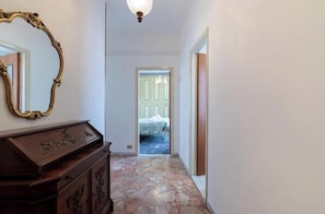 Un pasillo con un aparador de madera, un espejo y una puerta que da a una habitación con una cama.
