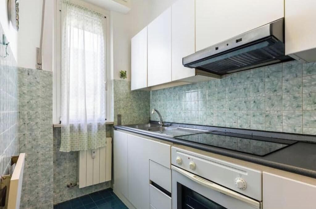 A kitchen with white cabinets, a black countertop, a stainless steel range hood, and a tiled backsplash.