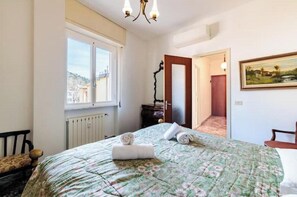 Un dormitorio con cama, ventana, radiador, puerta y un cuadro en la pared.