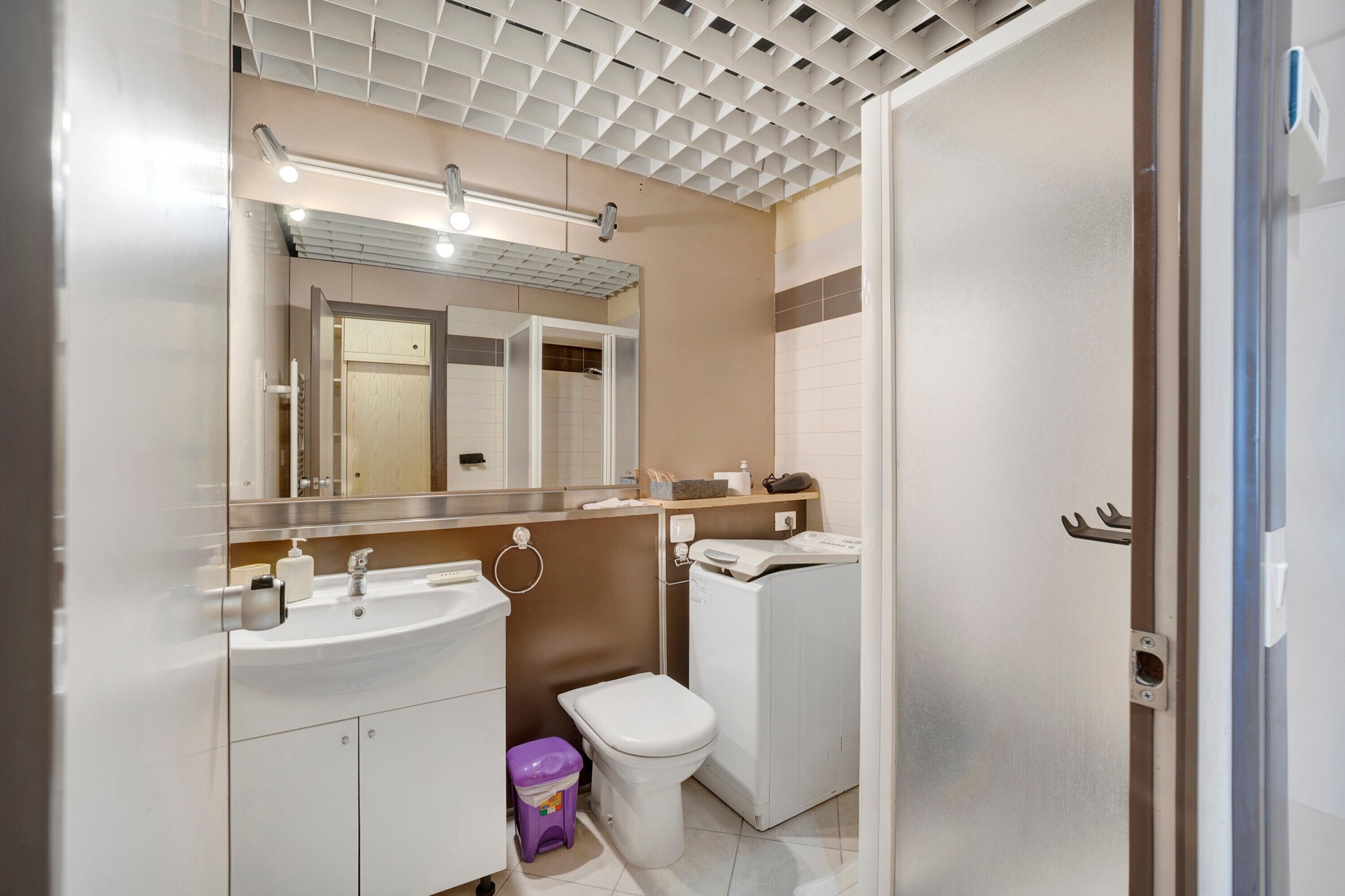 Une salle de bain moderne équipée d’un lavabo, d’un miroir, de toilettes et d’un lave-linge.