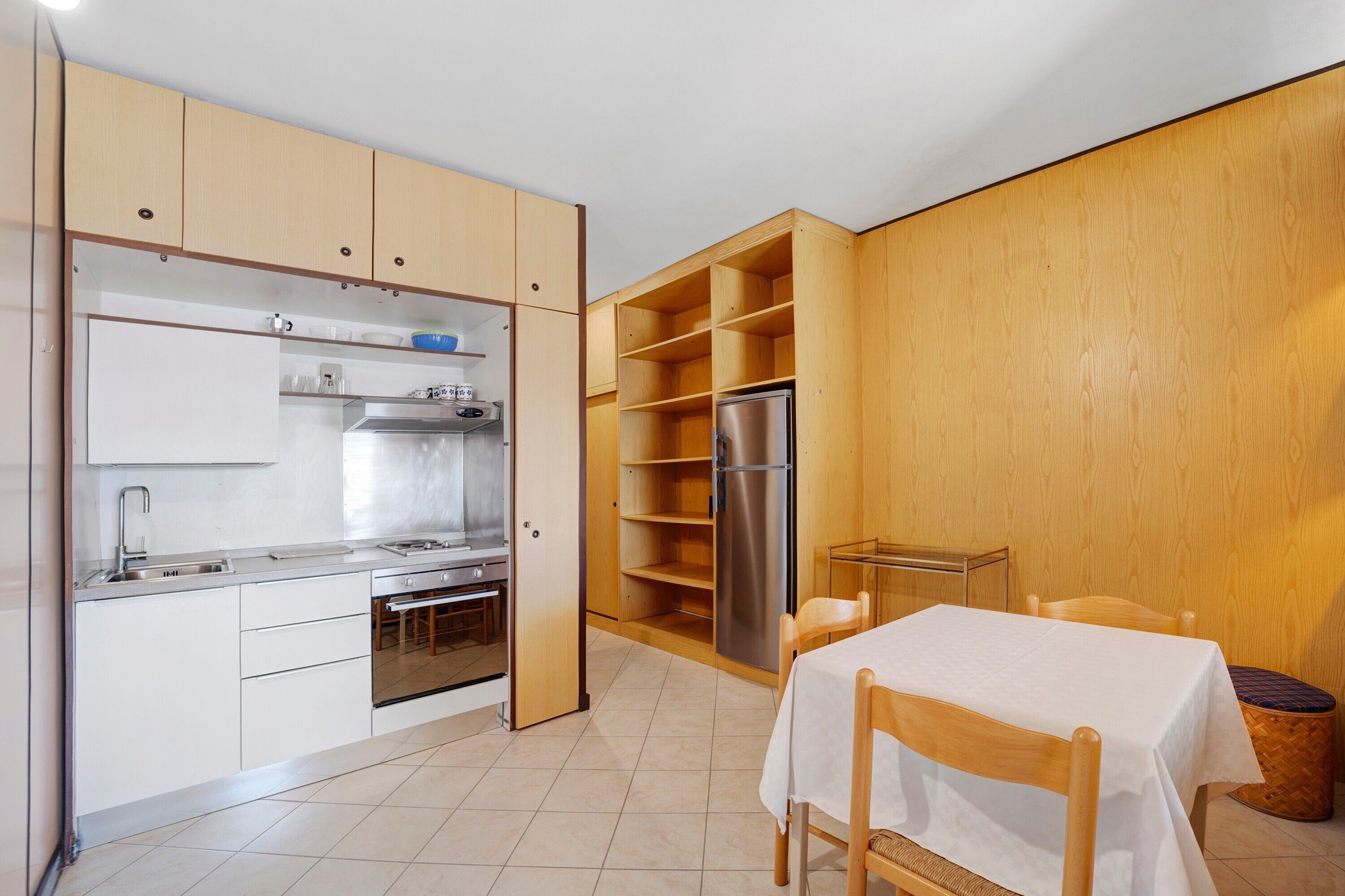 Uma cozinha compacta com forno embutido, geladeira e área de refeições com mesa e cadeiras.