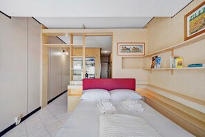 Ein Schlafzimmer mit einem Bett, einer roten Kopfteil, einem hölzernen Regal mit Büchern und einem Gemälde an der Wand.