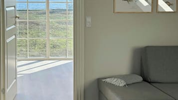 Une pièce avec un canapé gris, une grande fenêtre donnant sur la mer et des illustrations de poissons encadrées accrochées au mur.
