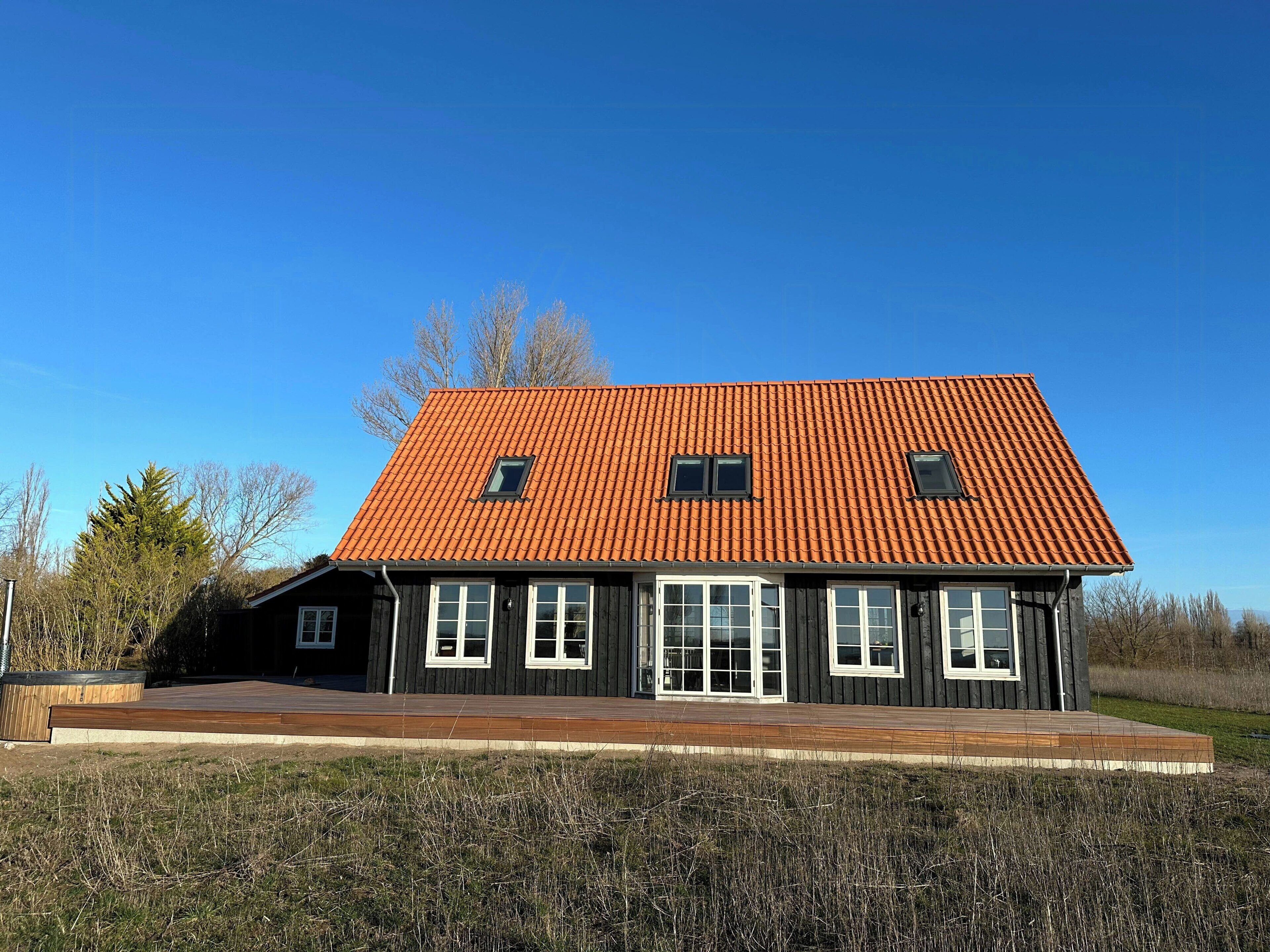 Een huis met twee verdiepingen, een rode pannendak, veel ramen en een houten terras.