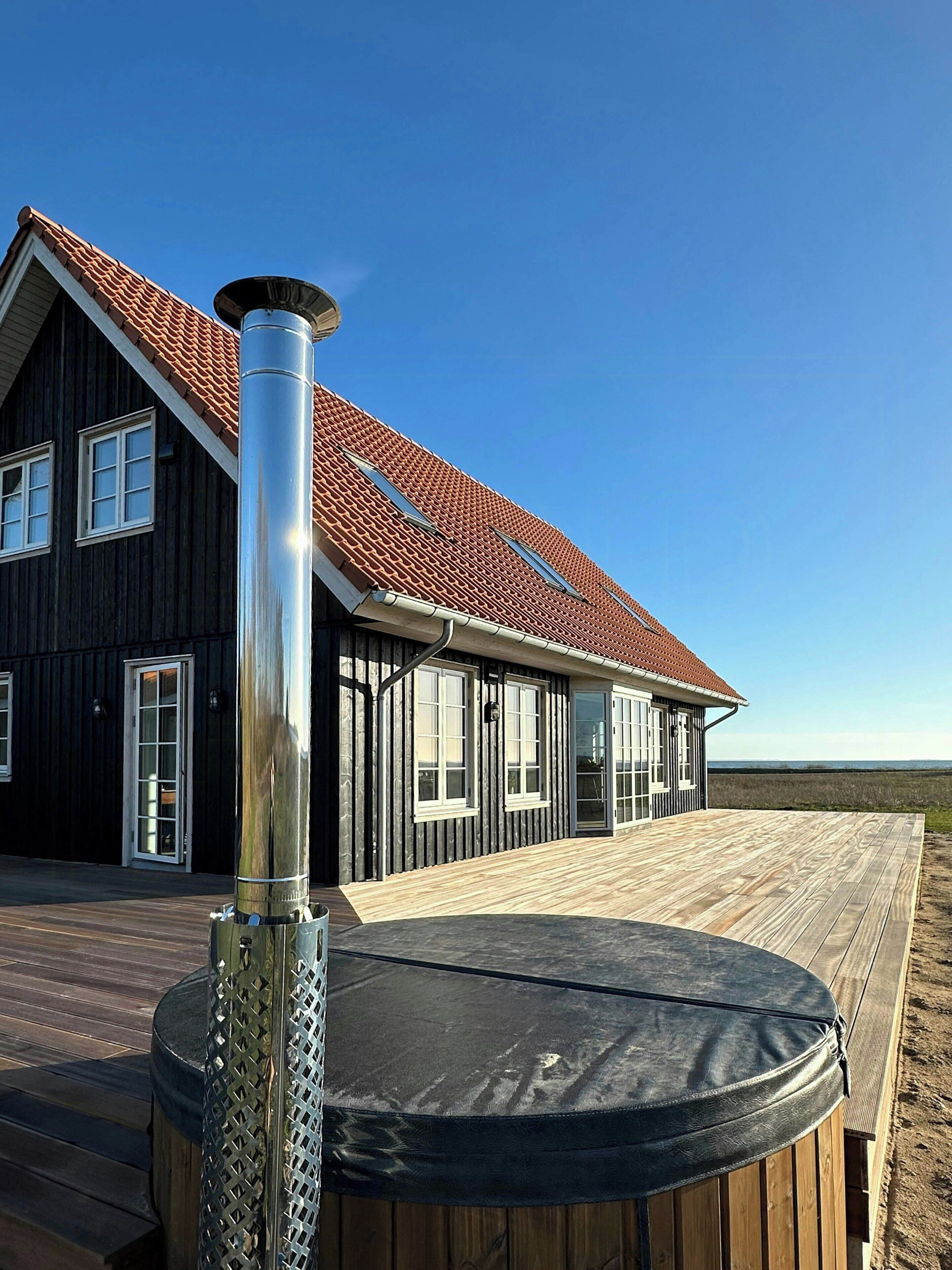 Une maison avec un toit recouvert de tuiles rouges, de grandes fenêtres et une terrasse en bois.