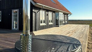 Ein Haus mit rotem Ziegeldach, großen Fenstern und einer Holzterrasse.