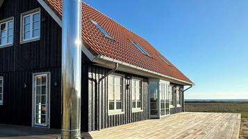 Une maison avec un toit recouvert de tuiles rouges, de grandes fenêtres et une terrasse en bois.