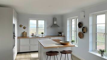 Une cuisine avec des meubles blancs, un plan de travail en bois, un îlot central avec des tabourets, une fenêtre offrant une belle vue et des assiettes décoratives accrochées au mur.