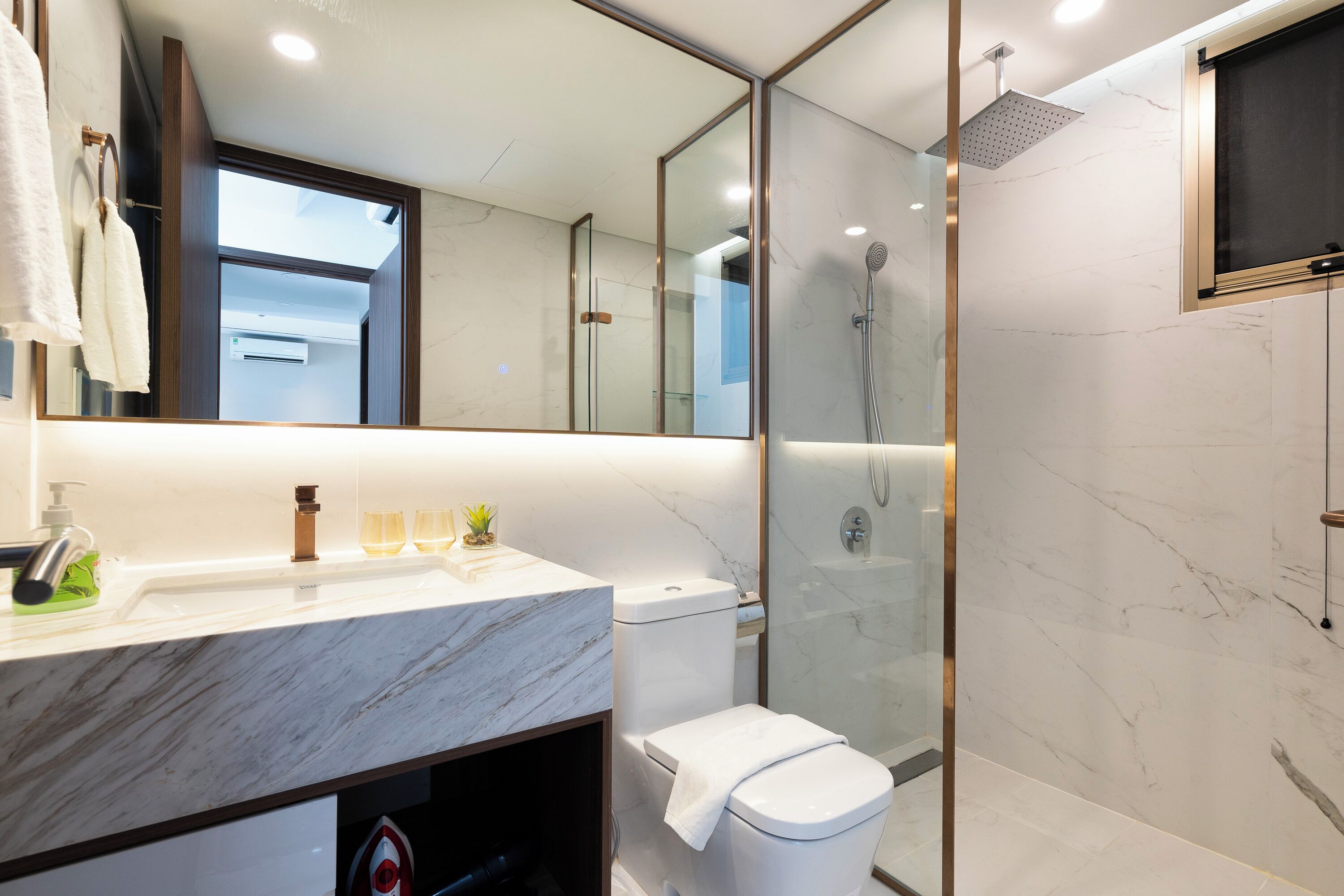 Un baño moderno con un lavabo de mármol, inodoro, ducha con mampara de vidrio y un espejo grande.