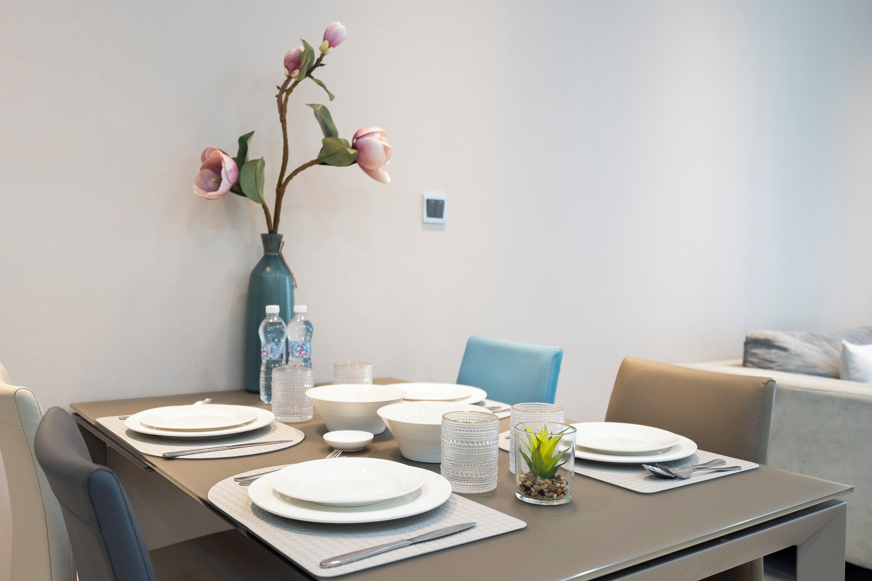 A dining table set with plates, cutlery, and a vase with flowers.