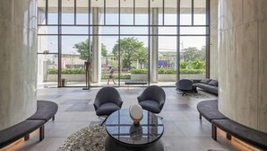 Eine moderne Lobby mit großen Fenstern, einem runden Tisch in der Mitte und Sitzbereichen.