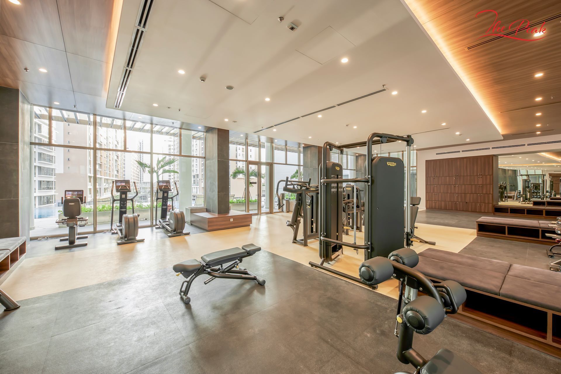 Un gimnasio moderno con diverso equipamiento de ejercicio, amplias ventanas y techo de madera.