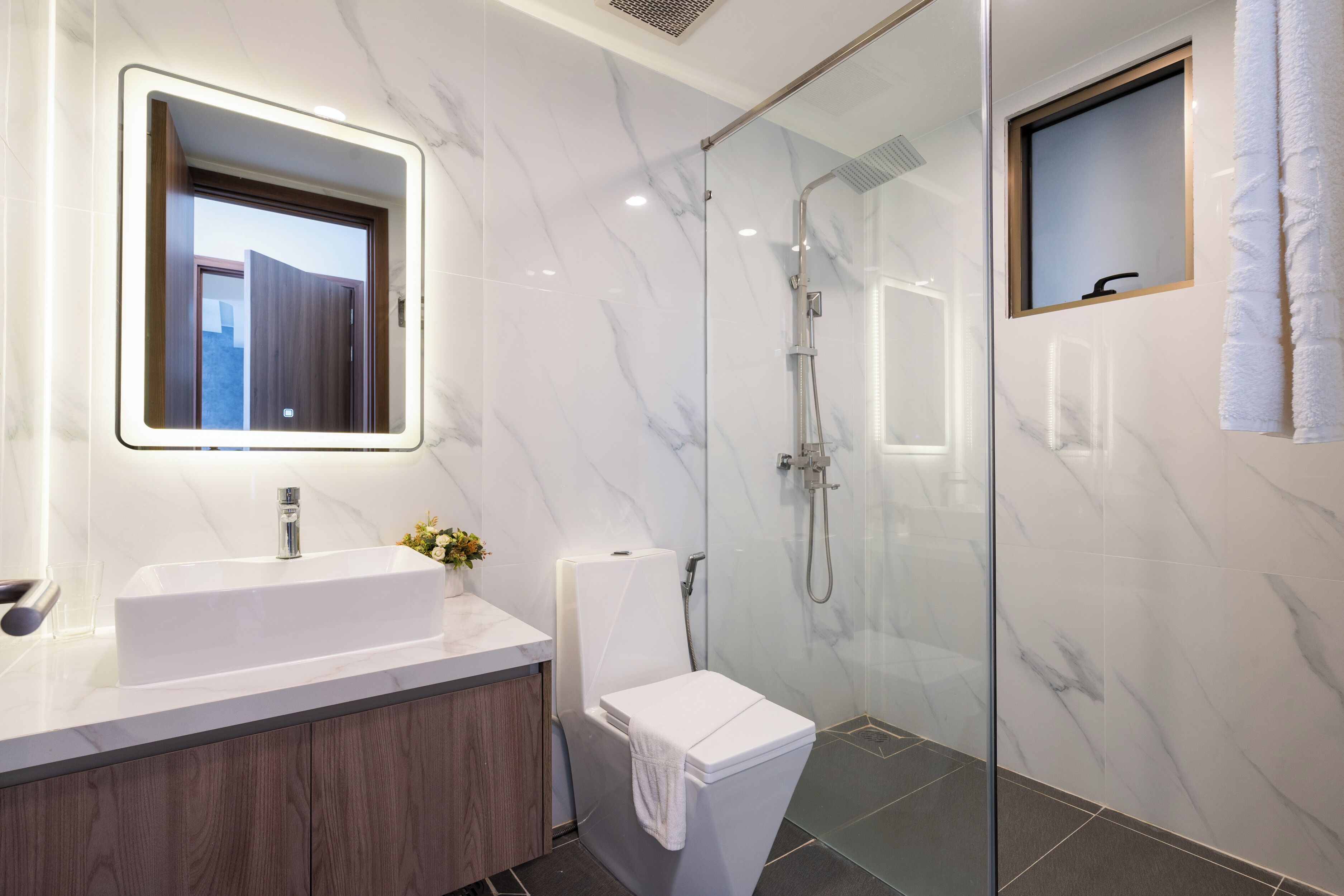 Un baño moderno con cabina de ducha de vidrio, un lavabo blanco y un espejo con marco de madera.