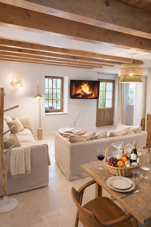 Ein gemütliches Wohnzimmer mit Kamin, einem Esstisch mit einer Obstschale und einer Couch.