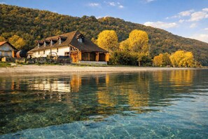 Ein Haus am See mit freiem Blick auf das Wasser, umgeben von Herbstbäumen und einer hügeligen Landschaft.