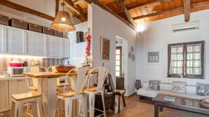 A kitchen with white cabinets, a wooden dining table, and bar stools. There is a sofa and a small table in the living area. - Peloponnese Beachfront Villa (Gelinas Beach house) (Paralia)
