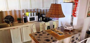 A compact kitchen with white cabinets, a microwave, a coffee maker, and a wicker lamp.