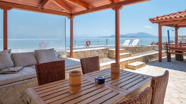 A covered outdoor seating area with a view of the sea, stone steps, and lounge chairs. - Peloponnese Beachfront Villa (Gelinas Beach house) (Paralia)